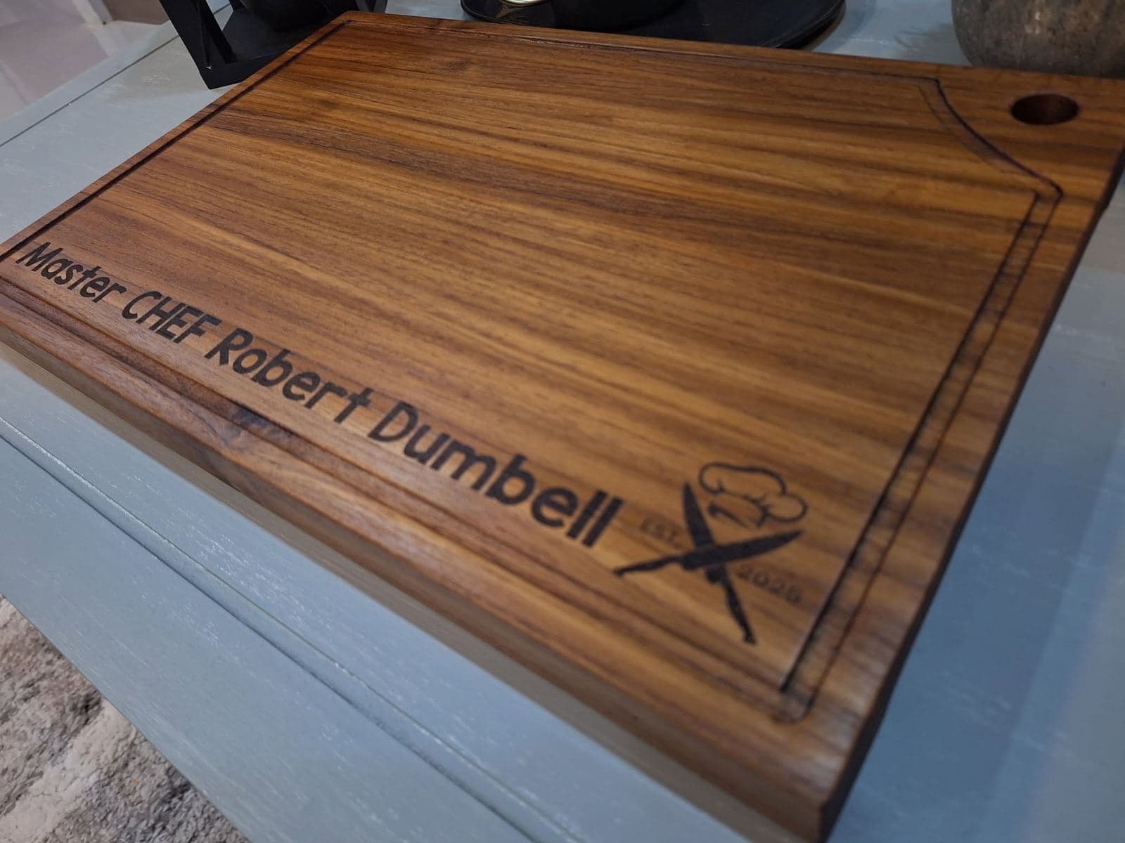 Hardwood cutting board with a juice groove and a laser-engraved chef's name and crossed knives