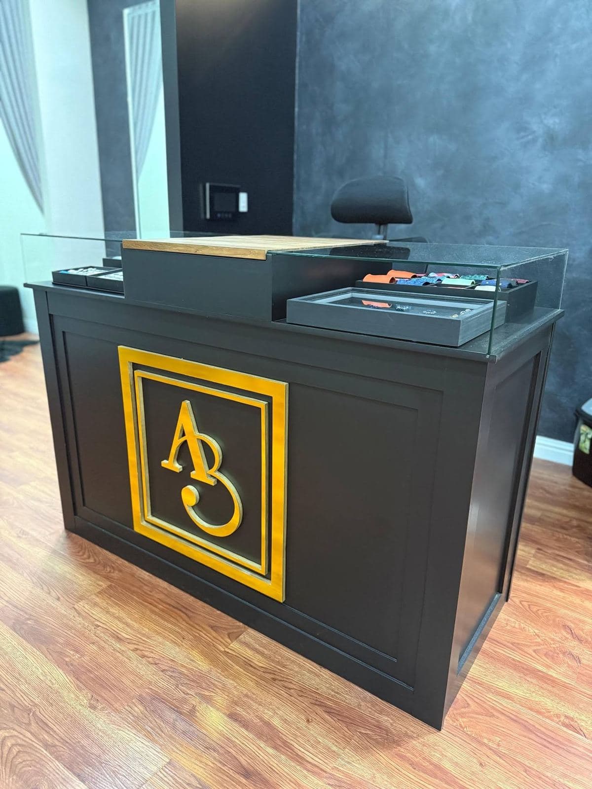 Black panelled reception counter with a raised gold monogram and glass display top