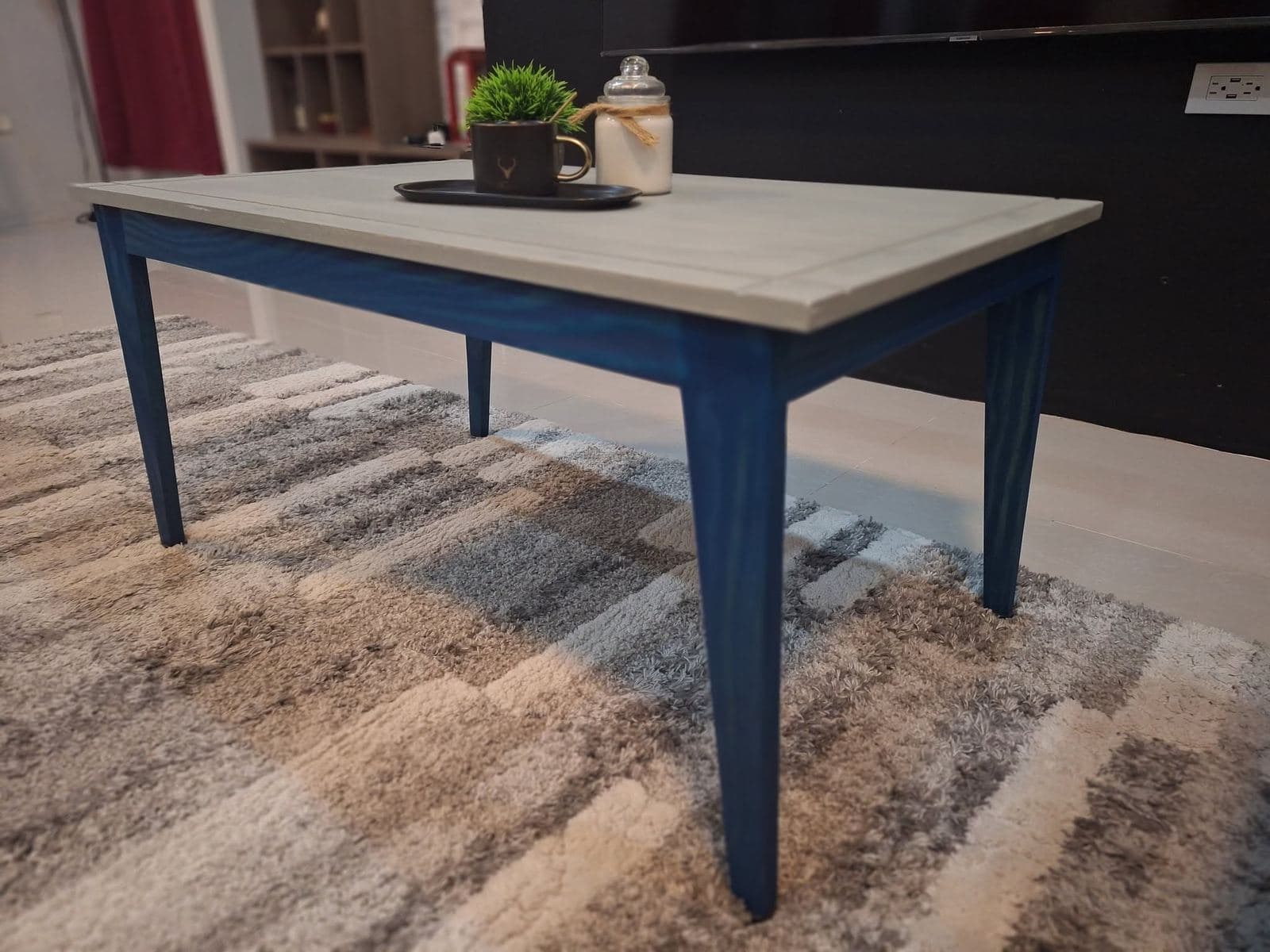 Coffee table with a weathered grey plank top and deep blue tapered legs on a patterned rug